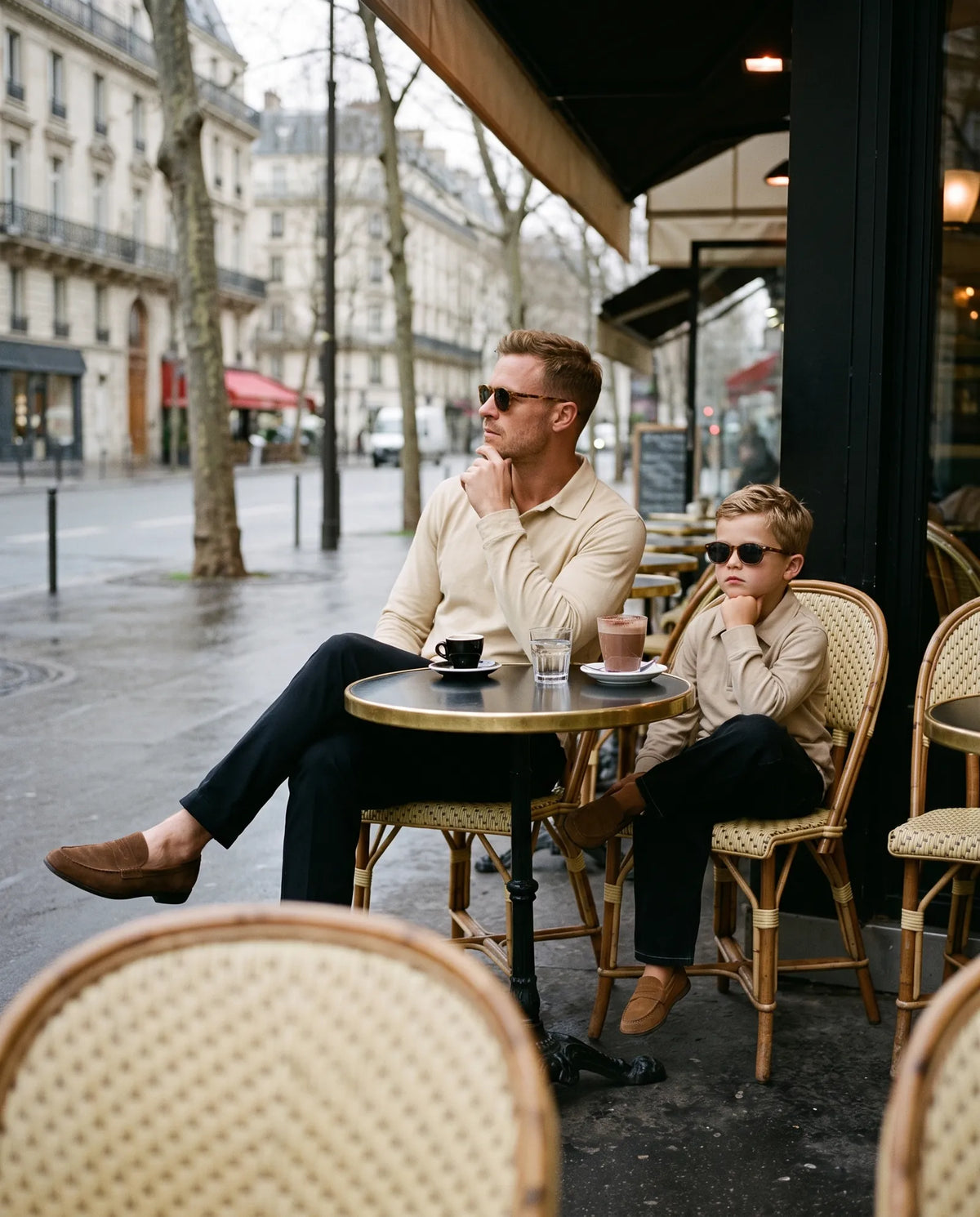Father and son at a Paris cafe terrace in beige long-sleeve polos, the boy copying his father's pose
