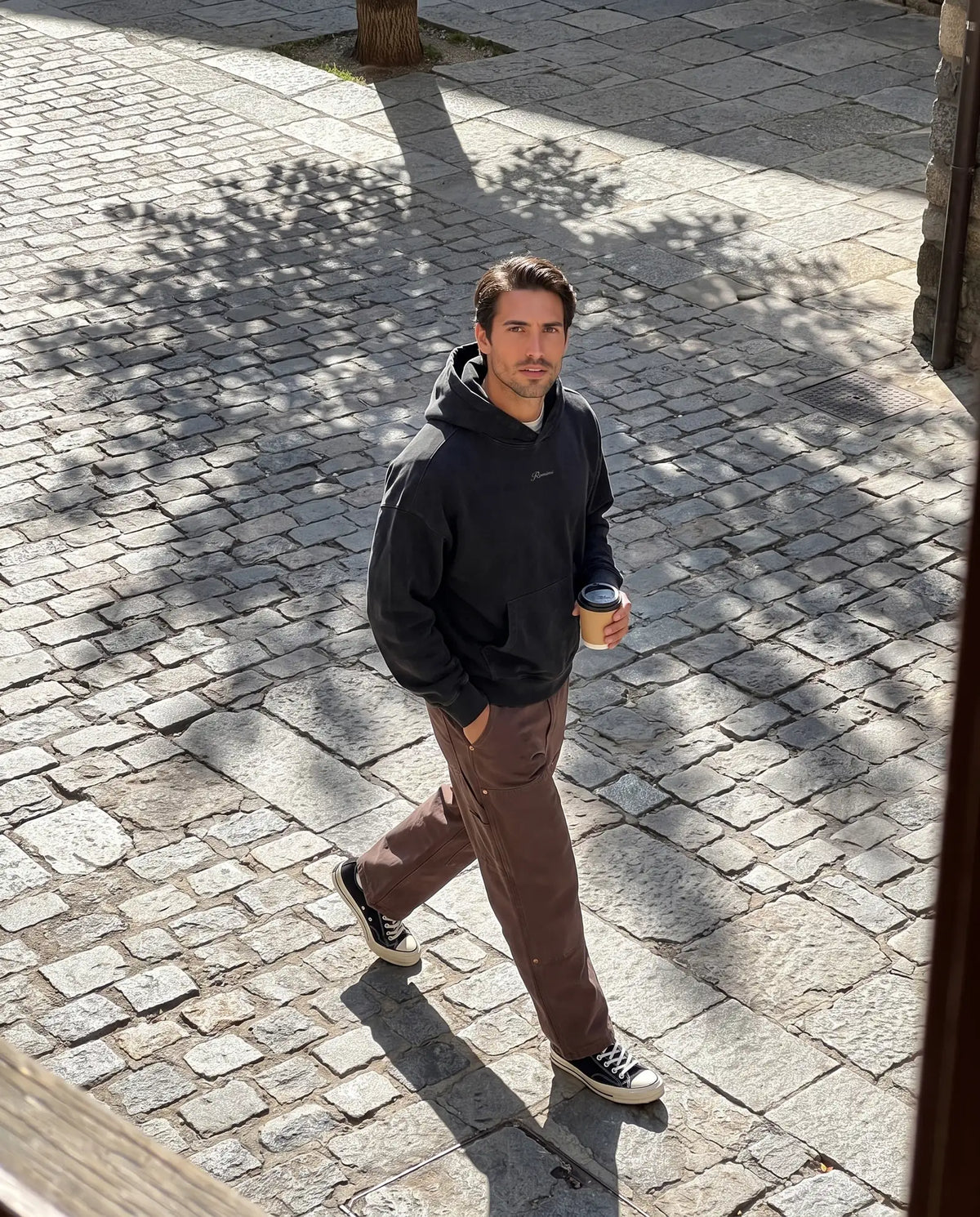 Man in the Romimi black hoodie and carpenter pants in a stone village street