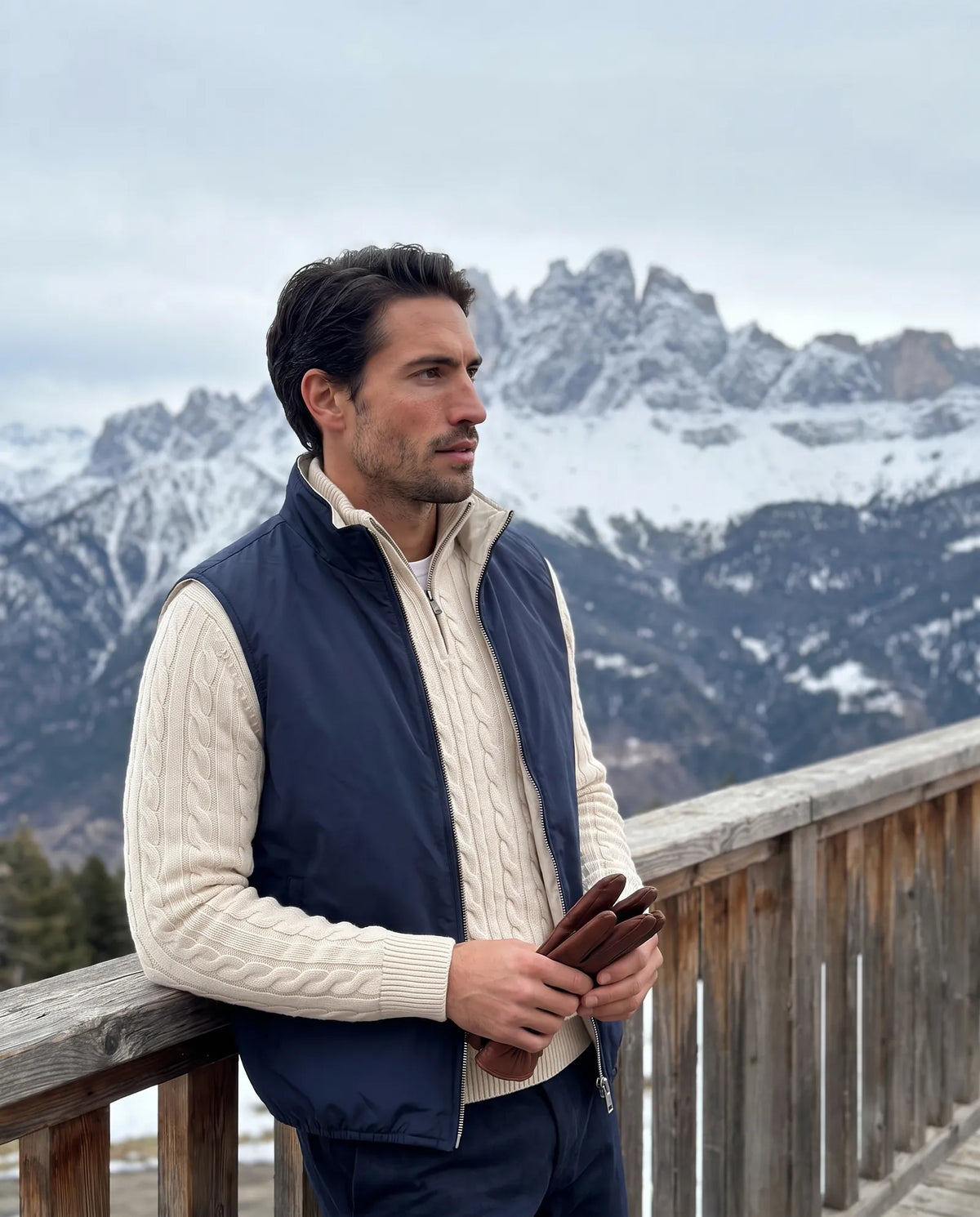 Man in a navy reversible gilet over an ecru cable-knit half-zip on a mountain balcony