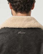 Detail of the Romimi aviator jacket in black with a cream collar: the silver metal Romimi logo below the collar