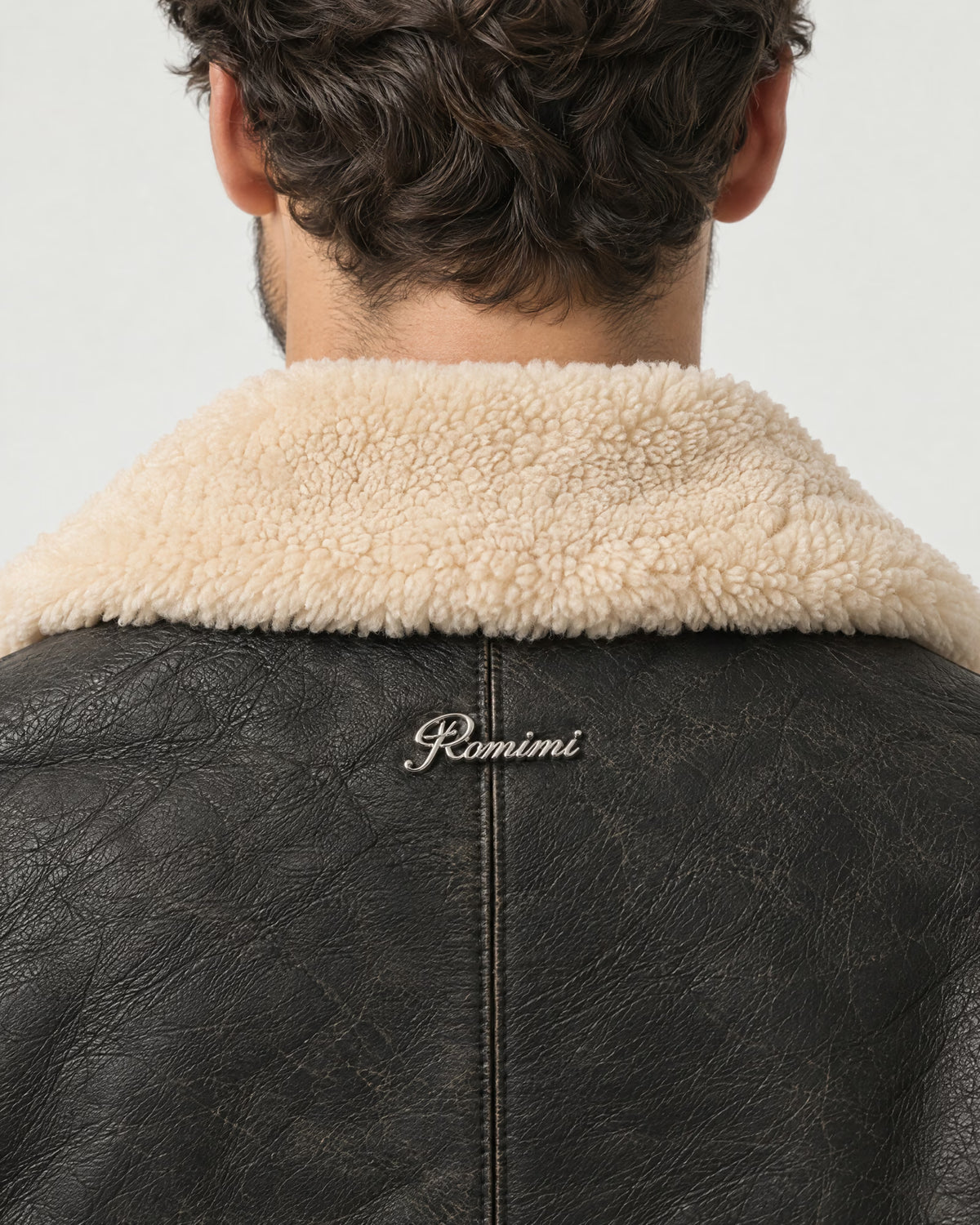 Detail of the Romimi aviator jacket in black with a cream collar: the silver metal Romimi logo below the collar