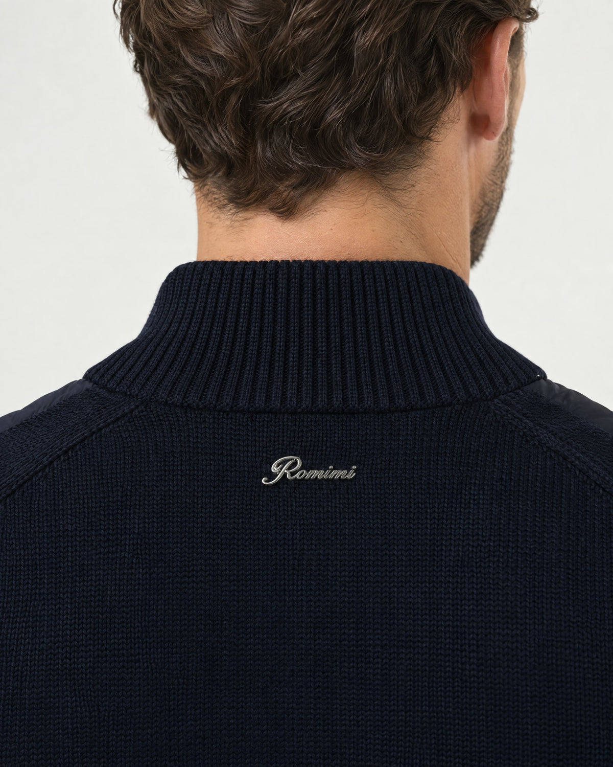 Detail of the Romimi padded knit cardigan in navy: the silver metal Romimi logo on the knitted back